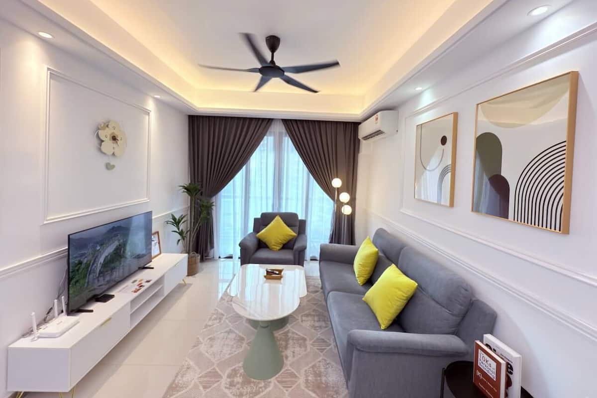 A modern living room with a flat-screen TV, a ceiling fan, a sofa with yellow pillows, and artwork on the walls.
