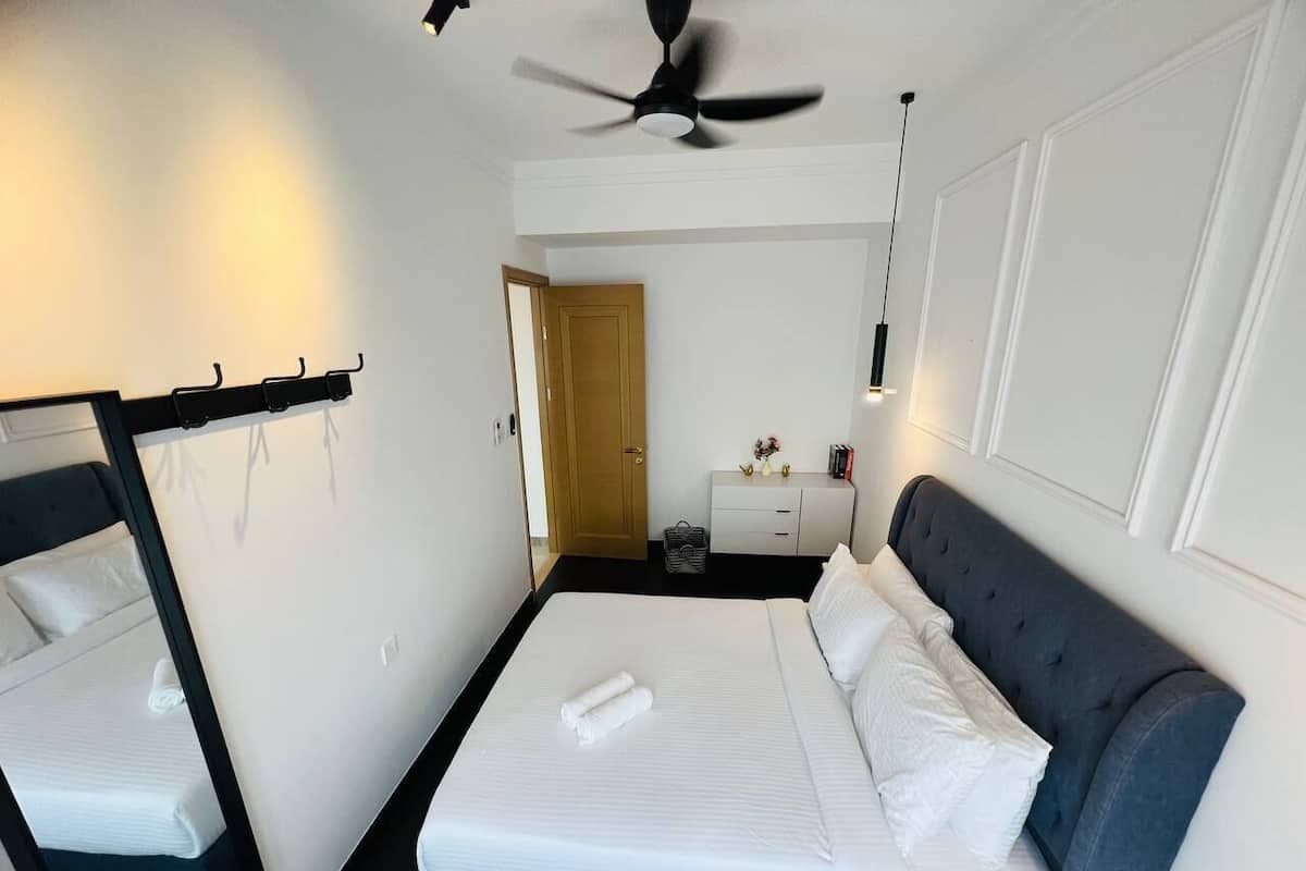 A neatly arranged hotel room with a bed, a bedside table, a mirror, and a ceiling fan.
