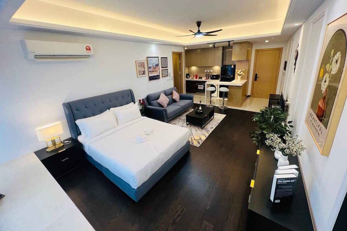 A modern hotel room with a large bed, a sofa, a desk, and a kitchenette.