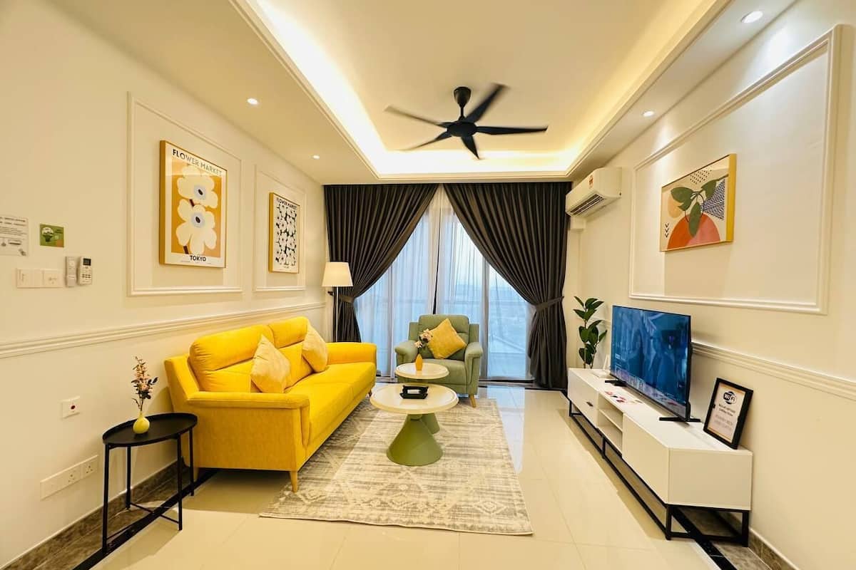 A modern living room with a yellow sofa, a green armchair, a TV, and artwork on the walls.