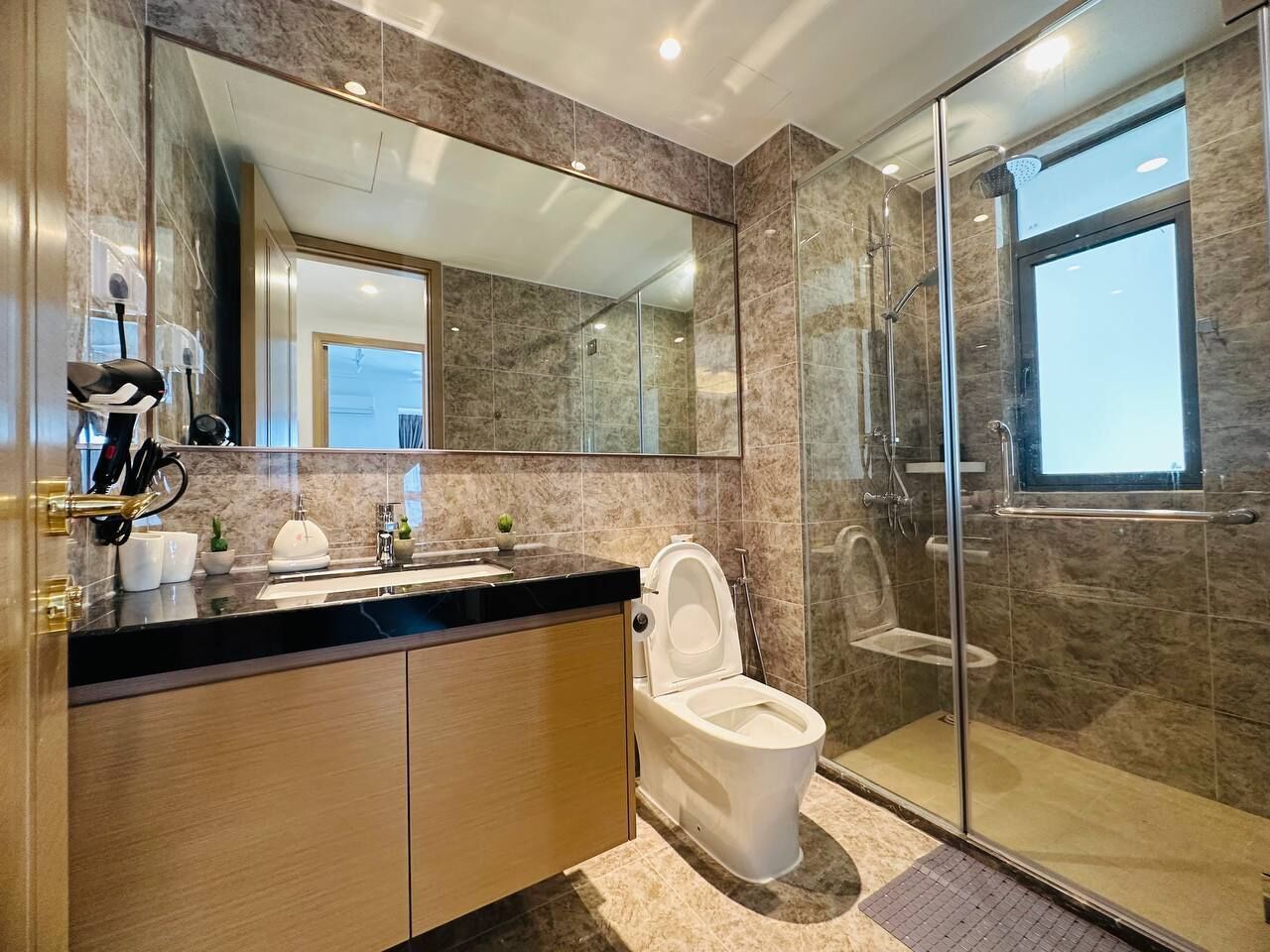 A modern bathroom with a marble vanity, a toilet, and a glass-enclosed shower.