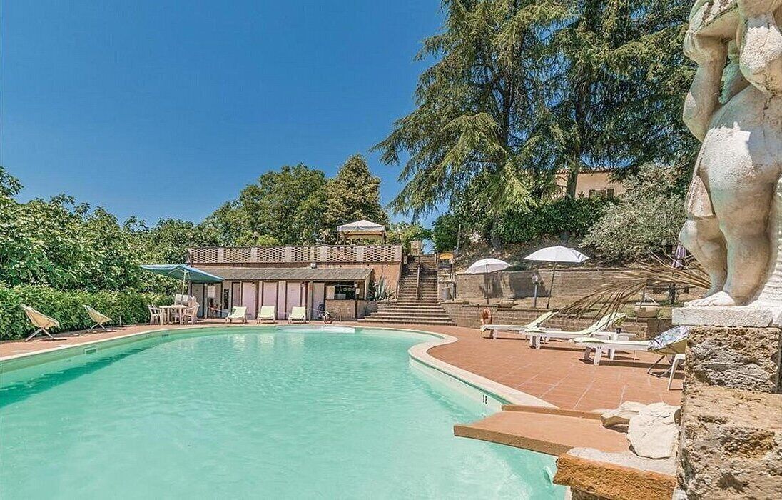 Una piscina con sillones de descanso y un edificio con zona cubierta.