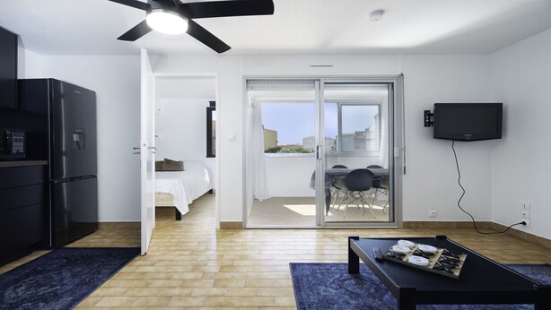 A compact living space with a kitchenette, a bed, a dining area, and a balcony with a view.