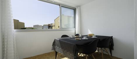 A dining area with a table set for two, a window with a view of buildings, and a curtain on the left.