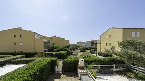 A residential area with beige buildings, a paved pathway, and well-maintained greenery.