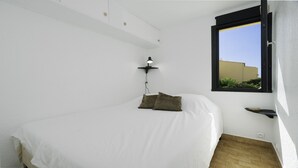 A bedroom with a bed, a bedside lamp, a window, and a small shelf.