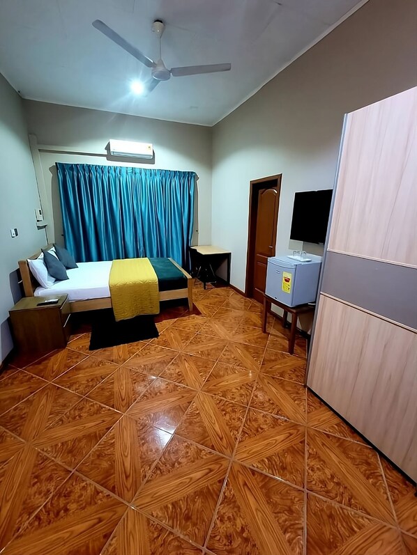 Una habitación de hotel con cama, escritorio, armario y ventilador de techo.