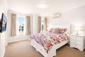 A well-lit bedroom with a large bed, a TV, and a window with curtains.