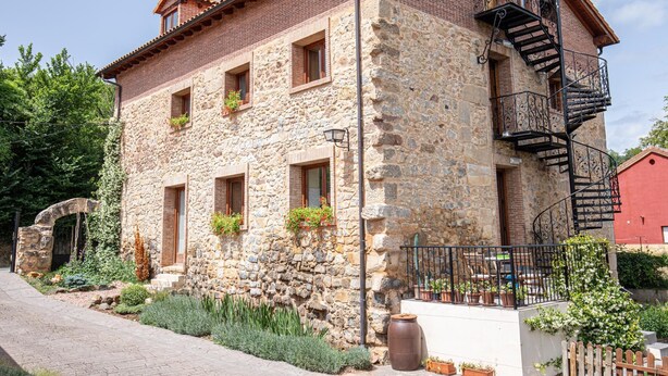 A stone building with a brick upper section, multiple windows, and a black spiral staircase. - Casa Rural en Terminon (Terminon)