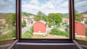 A view from a window with a wooden frame, overlooking a rural landscape with red buildings, greenery, and a clear sky. - Casa Rural en Terminon (Terminon)