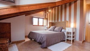 A bedroom with a sloped ceiling, a bed with a woven headboard, a bedside table, a wicker basket, and a window with curtains. - Casa Rural en Terminon (Terminon)