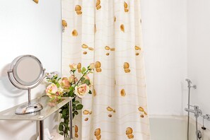 A bathroom with a vanity, a mirror, a vase with flowers, and a shower area.