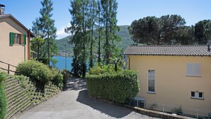 Un chemin menant à un bâtiment doté d’un toit en tuiles, entouré de verdure et offrant une vue sur un lac et des collines.