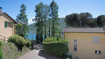 Ein Weg führt zu einem Gebäude mit Ziegeldach, umgeben von Grünflächen und mit Blick auf einen See und Hügel.