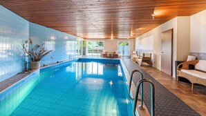 Une piscine dotée d’un plafond en bois et de murs carrelés, entourée de meubles en osier et agrémentée d’une porte.
