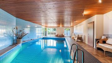 Ein Schwimmbecken mit Holzboden und gefliesten Wänden, umgeben von Korbmöbeln und einer Tür.
