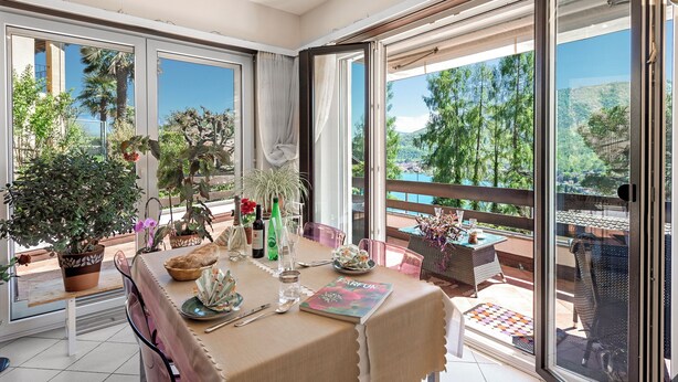 Un coin repas avec une table dressée pour deux personnes, des plantes en pot et une vue sur l’extérieur.