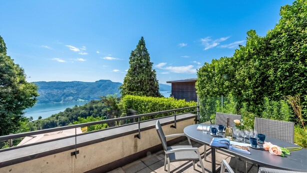 A terrace with a table set for dining, overlooking a scenic landscape with mountains and a lake. - Vernate Lugano Lake Sweet View (Vernate)