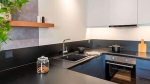 Une cuisine moderne avec un plan de travail noir, des appareils en acier inoxydable et des armoires blanches.