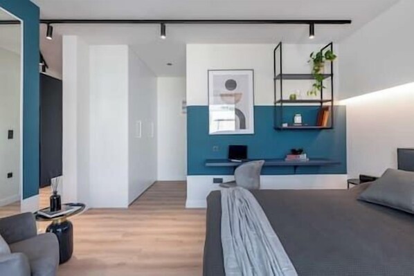 A modern bedroom with a large bed, a desk, and a wall-mounted shelf with a plant.