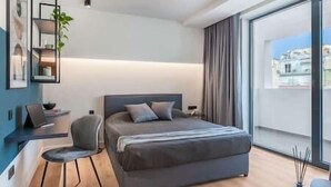 Une chambre moderne avec un grand lit, un bureau et une chaise. Une grande fenêtre offre une vue sur la ville.