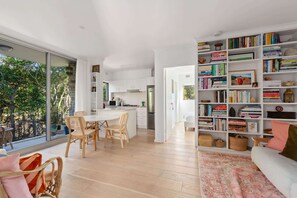 A modern open-plan living space with a kitchen, dining area, and a large bookshelf filled with books. - Lovely Harbourside 1-Bed Close To Sydney Landmarks (Kurraba Point)