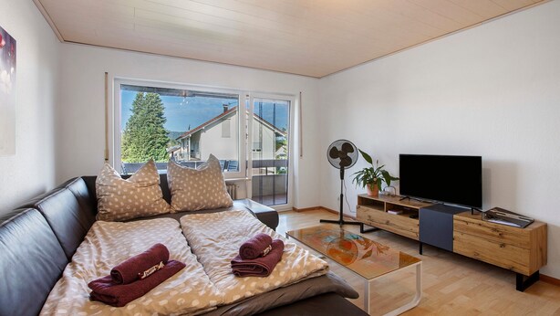 Een moderne woonkamer met een bank, een flatscreen televisie, een salontafel en een schuifdeur die leidt naar een balkon.