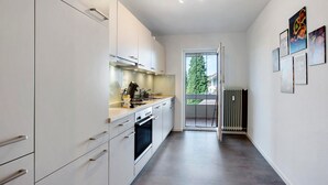 Een moderne keuken met witte kasten, een inbouwoven en uitzicht op de omgeving door een glazen deur.