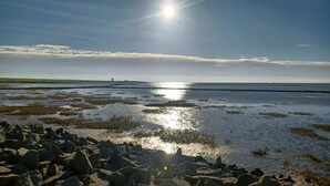 A coastal landscape with a clear sky, sunlight reflecting on water, and a distant horizon.