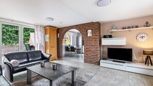 A living room with a leather sofa, a coffee table, a flat-screen TV, and a brick wall.