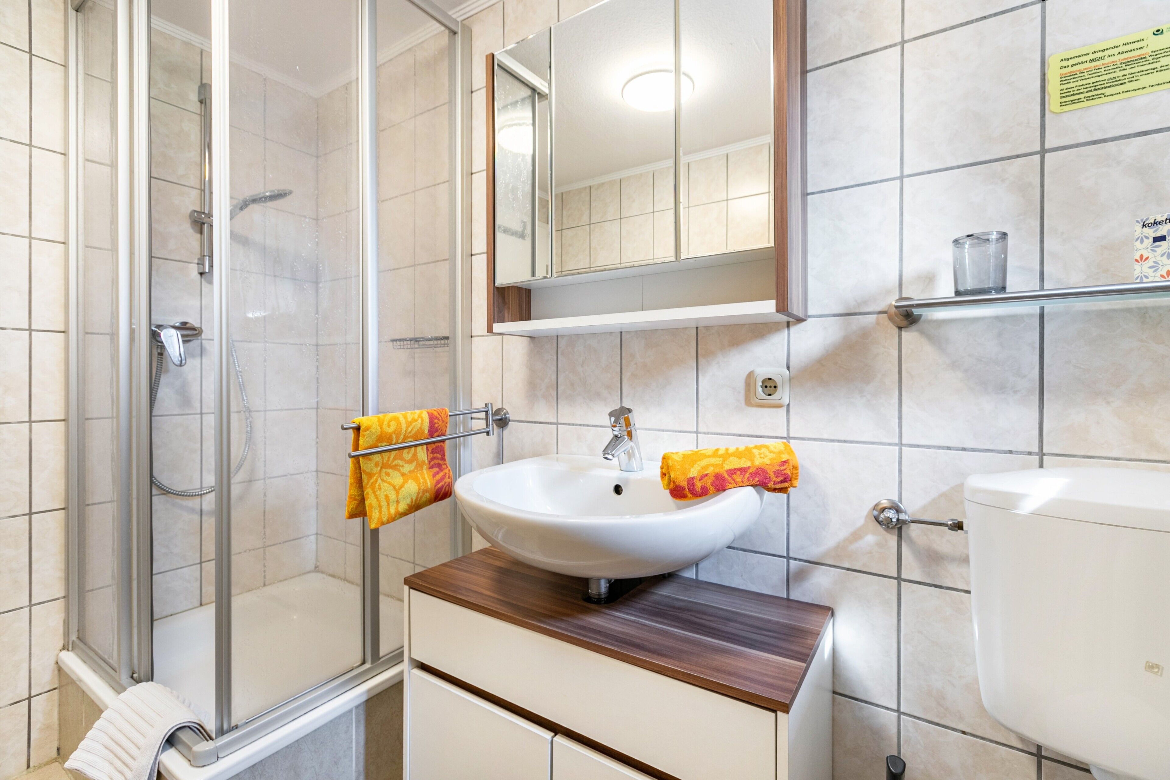 Un baño con cabina de ducha de vidrio, un lavabo blanco con encimera de madera, un espejo sobre el lavabo y un inodoro.