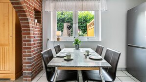 A dining area with a brick wall, a window with a view of greenery, a table set for four, and a modern refrigerator.