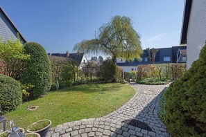 Un chemin pavé dans une cour, avec un saule pleureur, des haies soigneusement taillées et un petit étang.