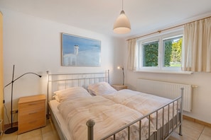 Une chambre à coucher avec un lit, une table de chevet, une lampe et une fenêtre avec des rideaux.