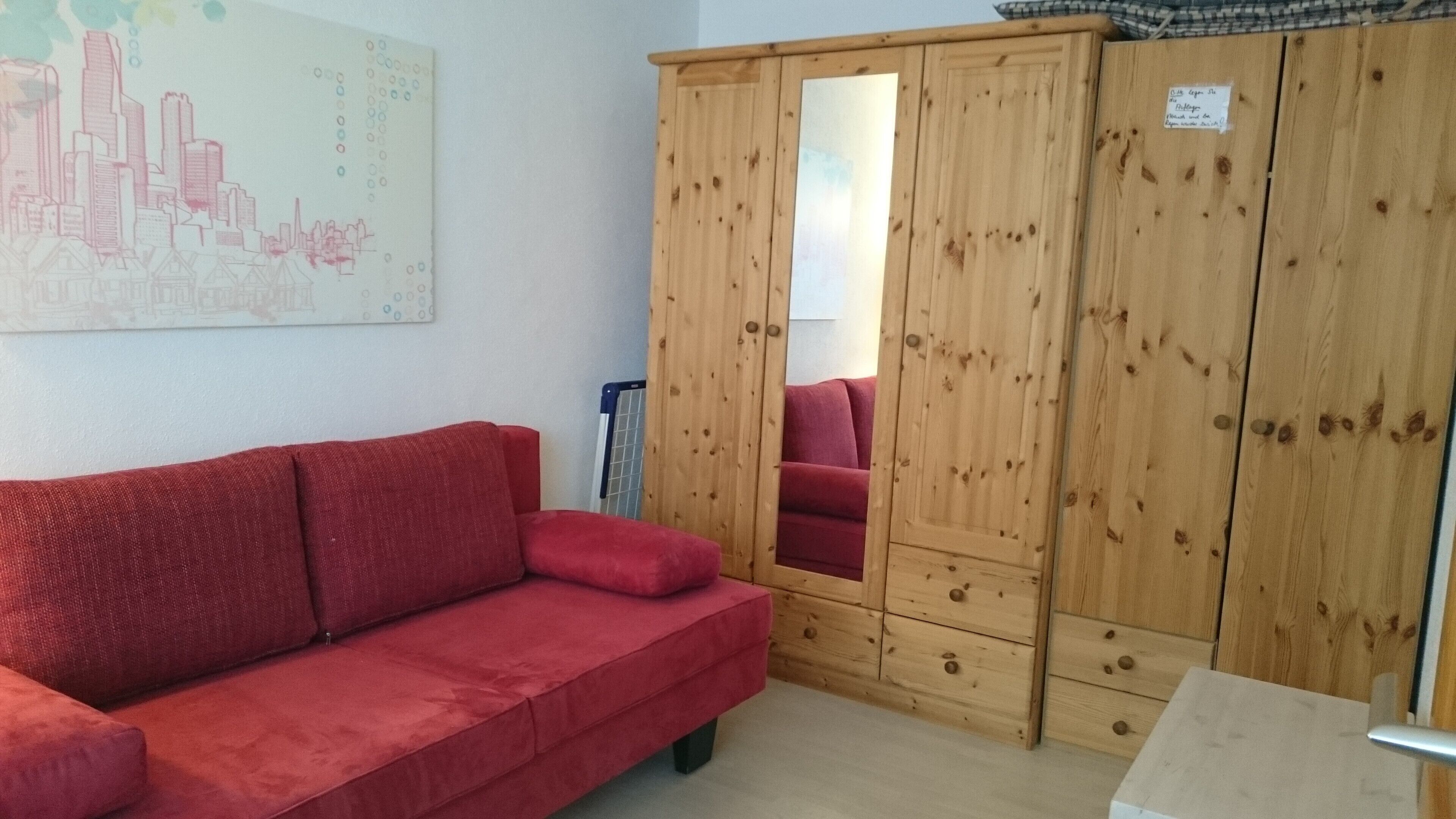 En röd soffa, ett träskåp och en målning som föreställer en stadsbild i ett rum.