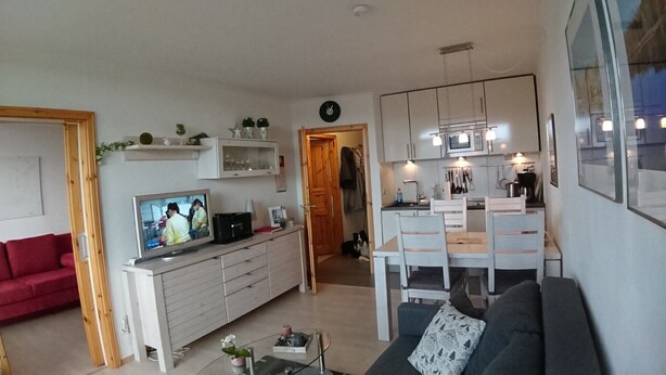 Un espace de vie compact comprenant un téléviseur, un canapé, une kitchenette et une porte donnant sur une autre pièce.