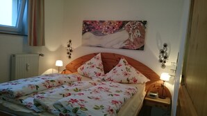 Une chambre à coucher avec un lit, une literie à motifs floraux, un tableau au mur, des lampes de chevet et un radiateur.