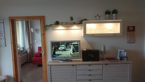 Un salon comprenant un téléviseur, un canapé rouge, un meuble en bois et une porte donnant sur une autre pièce.