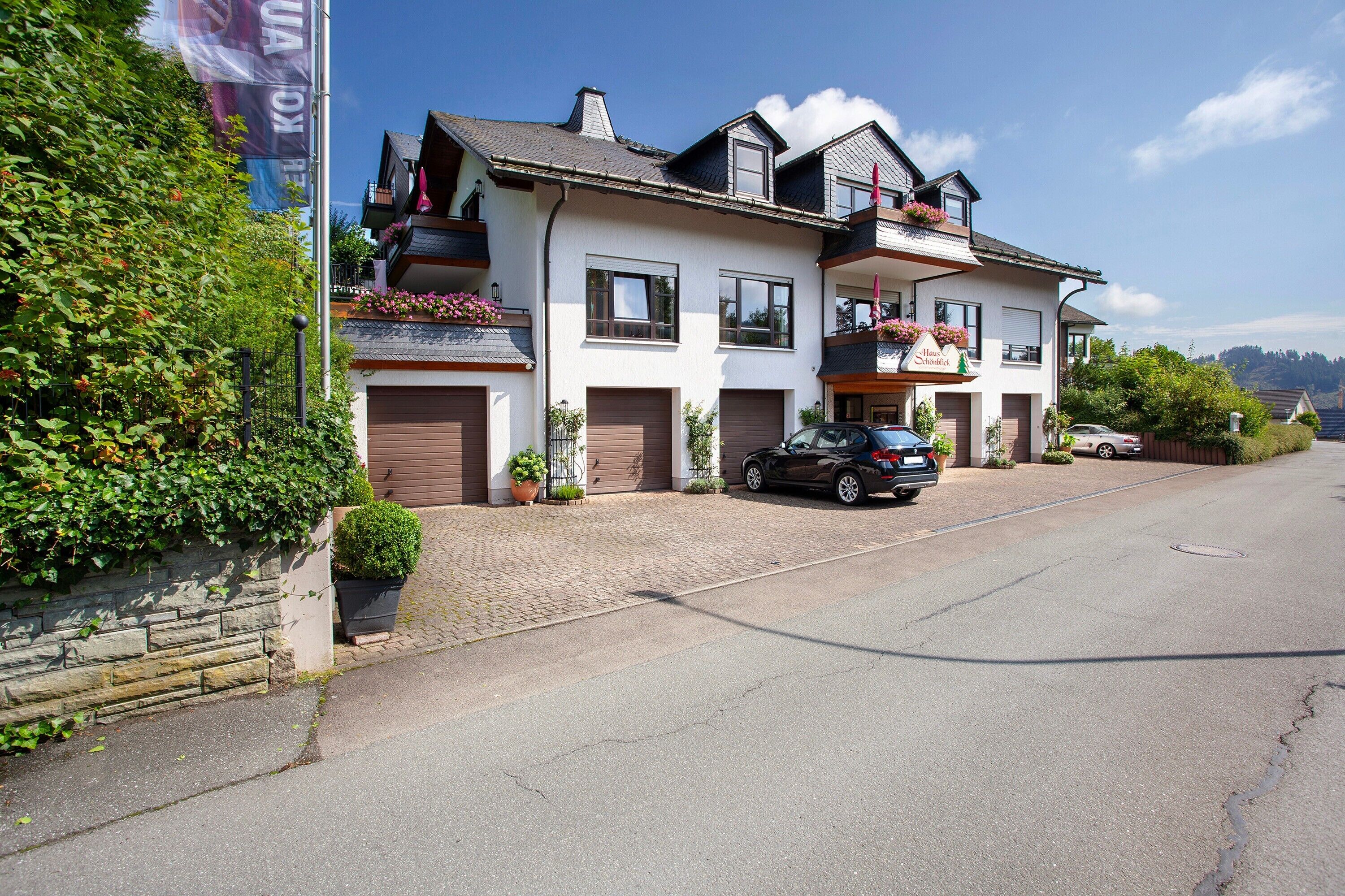 A two-story building with a garage, a balcony with flowers, and a car parked in front.