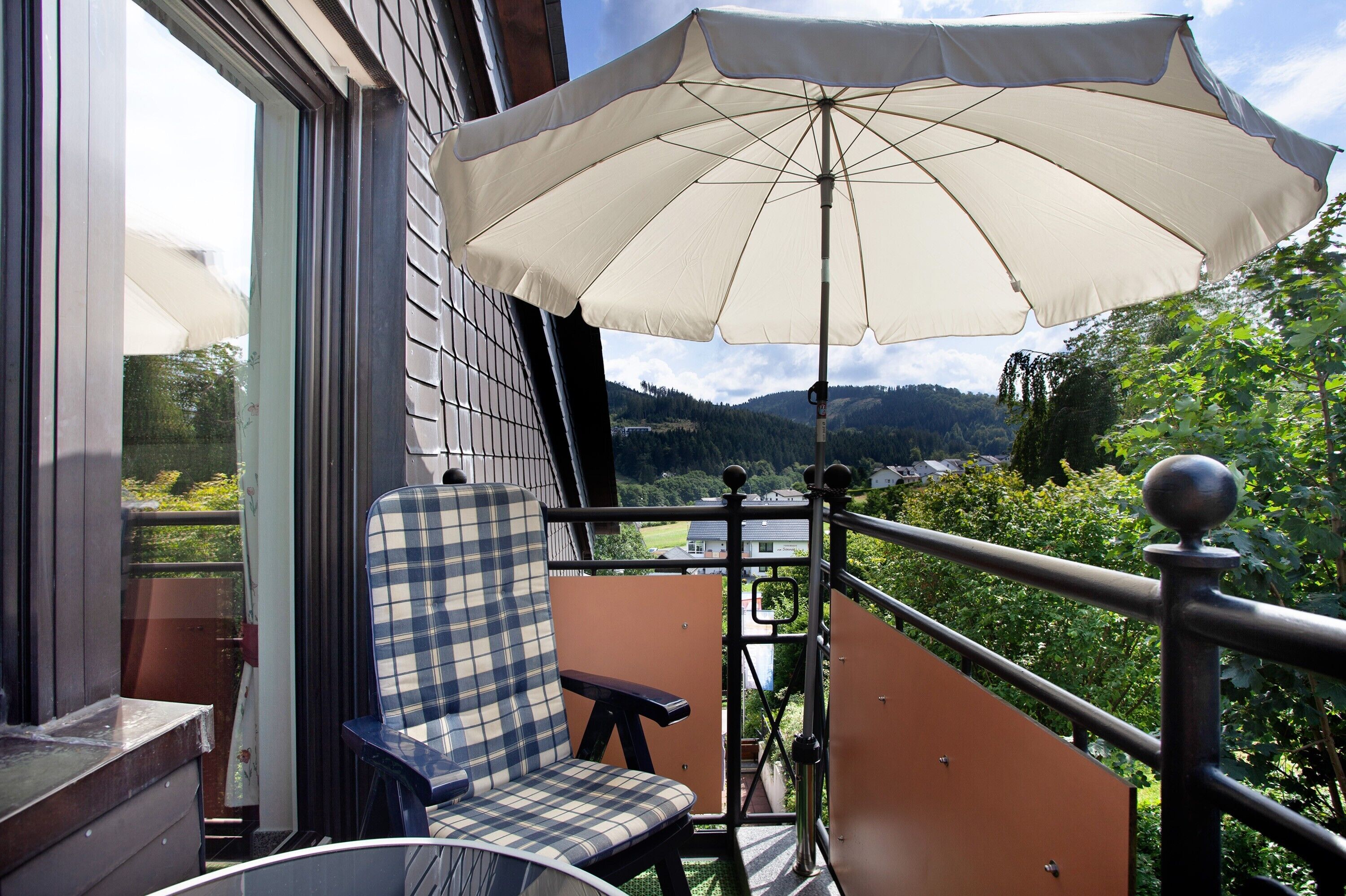 Un balcon avec une chaise, un parasol et une vue sur un paysage montagneux.