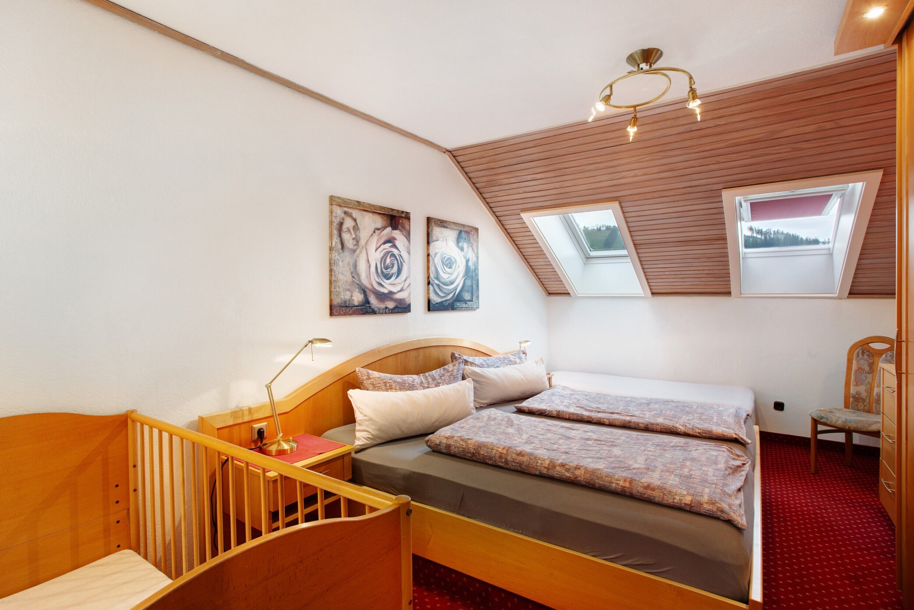 A bedroom with a wooden bed, a desk, a chair, and a skylight.