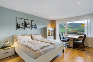 A bedroom with a bed, bedside tables, a desk with chairs, and a window with a view.