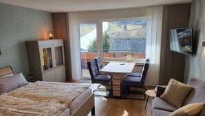 A hotel room with a bed, a desk with two chairs, a television, and a view of the outdoors. - Haus Schönblick – Apartment 3 with Mountain View, Balcony and Wi-Fi (Willingen (Upland))