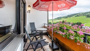 A balcony with a red umbrella, a table, chairs, and a flower box with pink flowers. - Haus Schönblick – Apartment 3 with Mountain View, Balcony and Wi-Fi (Willingen (Upland))