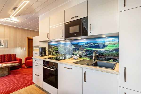 A modern kitchen with white cabinets, a black microwave, and a large window with a scenic view.