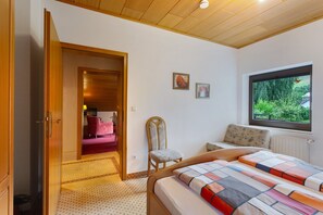 Une chambre à coucher comprenant un lit, une chaise, une fenêtre et une porte donnant sur une autre pièce.