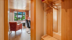 Un interior de madera con una silla roja, un banco de madera y un perchero con ropa doblada.