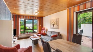 Una sala de estar moderna con techo de madera, un sofá gris, una mesa de comedor y un televisor.