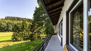 A building with large windows, a balcony, and a view of a forested area.