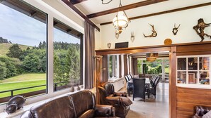 A spacious living area with leather sofas, a dining table, and a view of a green landscape through large windows.